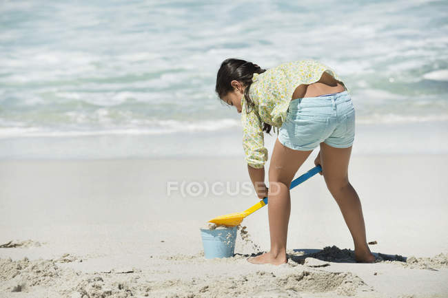 Visão traseira da menina jogando na praia de areia com balde de areia e pá — Fotografia de Stock