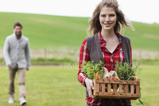 Mujer sosteniendo cesta de verduras con marido recogiendo leña en el campo - foto de stock