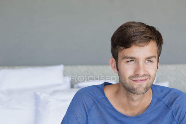 Крупный план улыбающегося молодого человека, сидящего на кровати — стоковое фото