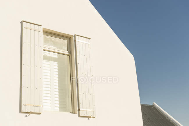 Вікно з рулонними шторами та фасадом білого будинку на тлі чистого неба — стокове фото