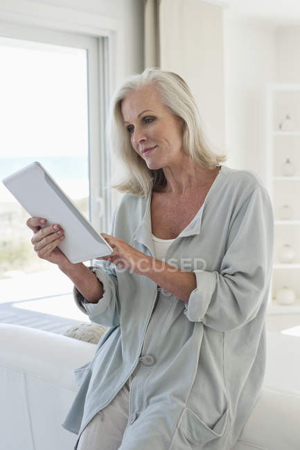 Donna anziana utilizzando tablet digitale e a casa — Foto stock