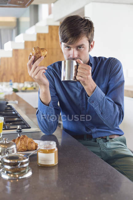 Чоловік снідає за кухонною стійкою і дивиться на камеру — стокове фото