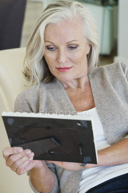 Senior femme regardant cadre photo tandis que assis sur canapé à la maison — Photo de stock