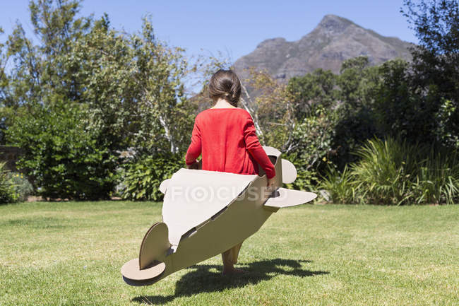Маленька дівчинка грає з картонним літаком на газоні — стокове фото