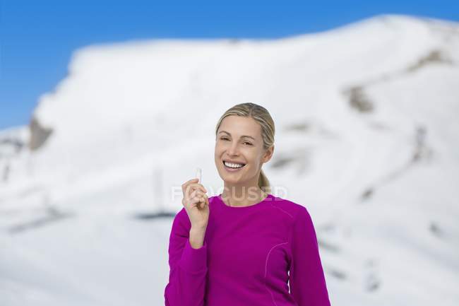 Portrait of happy woman holding lip balm in snowy mountains — Stock Photo
