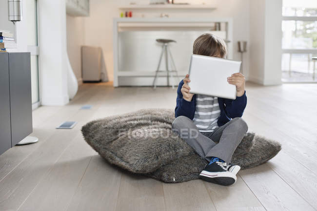 Хлопчик ховається обличчям з цифровим планшетом в сучасній квартирі — стокове фото