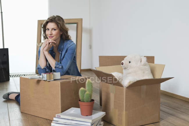 Портрет улыбающейся женщины, опирающейся на картонную коробку — стоковое фото
