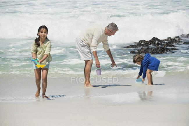 Niños jugando con su abuelo en la playa - foto de stock