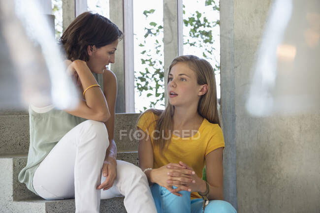 Mother and daughter sitting on steps and talking to each other — Stock Photo