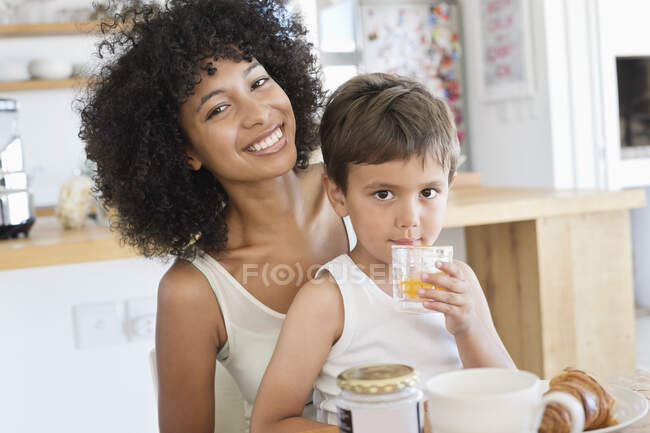 Мальчик пьет апельсиновый сок с матерью, сидящей рядом с ним — стоковое фото
