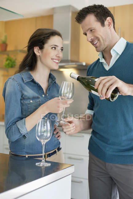Coppia sorridente versando vino in vetro in cucina — Foto stock