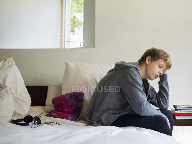 Підлітковий хлопчик сидить на ліжку і думає — стокове фото