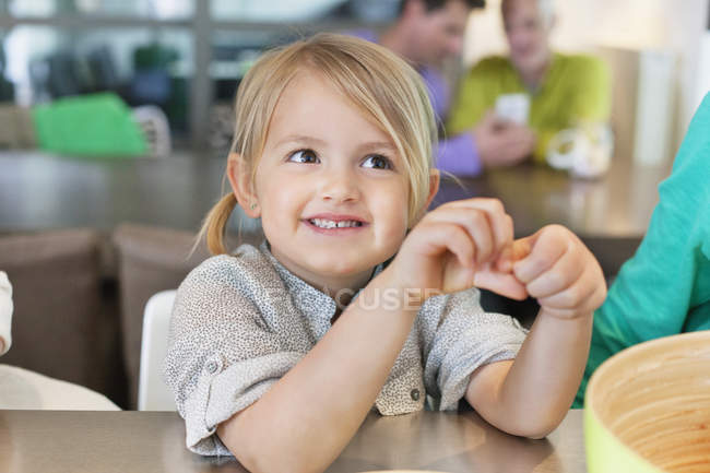Усміхнена мила дівчинка сидить на столі вдома — стокове фото
