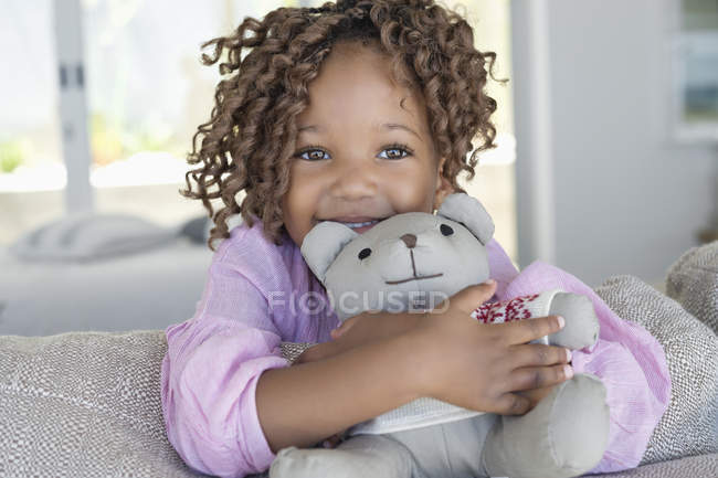 Portrait of smiling little girl holding teddy bear in room — Stock Photo