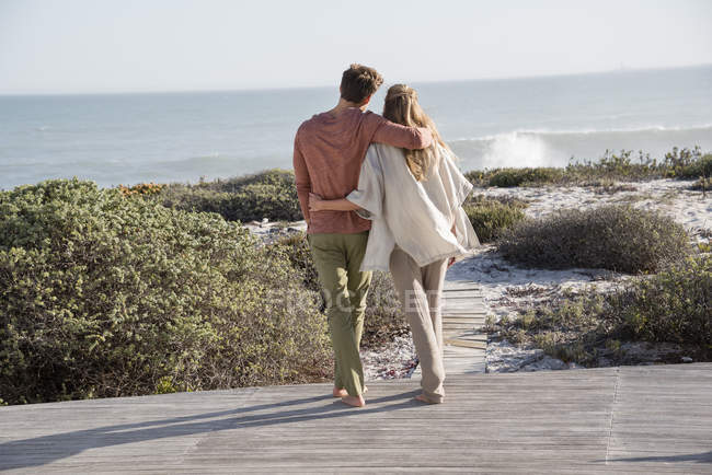 Romantic couple walking on coast with vegetation in sunlight — Stock Photo