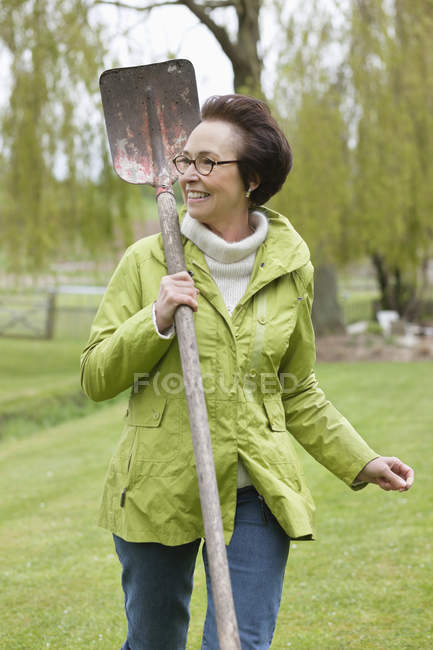 Smiling senior woman walking with spade in park and looking away — Stock Photo