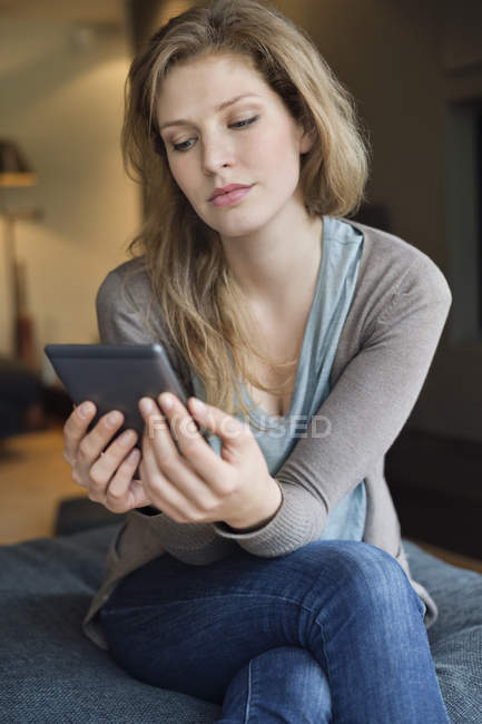 Serious woman using digital tablet on sofa in room — Stock Photo