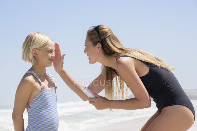 Mulher bonita aplicando protetor solar em seu rosto filha — Fotografia de Stock