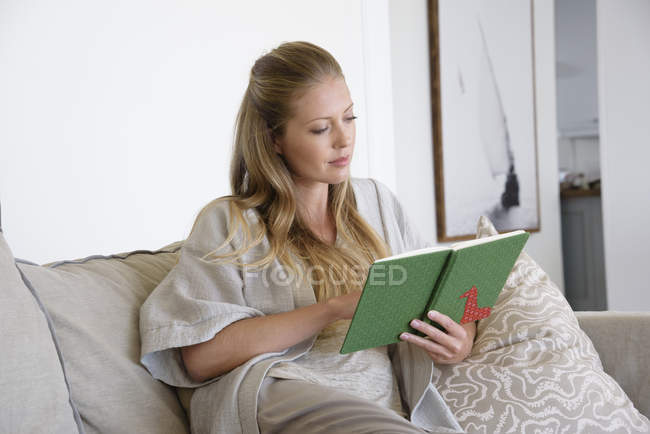 Fokussierte Frau liest Buch zu Hause auf dem Sofa — Stockfoto