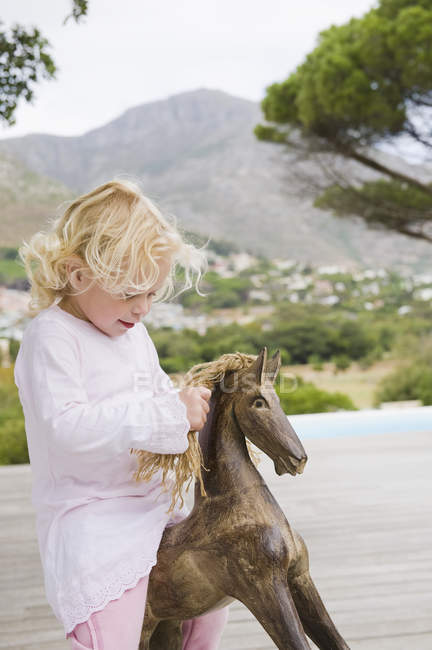 Linda niña jugando con un caballo mecedora en la naturaleza - foto de stock