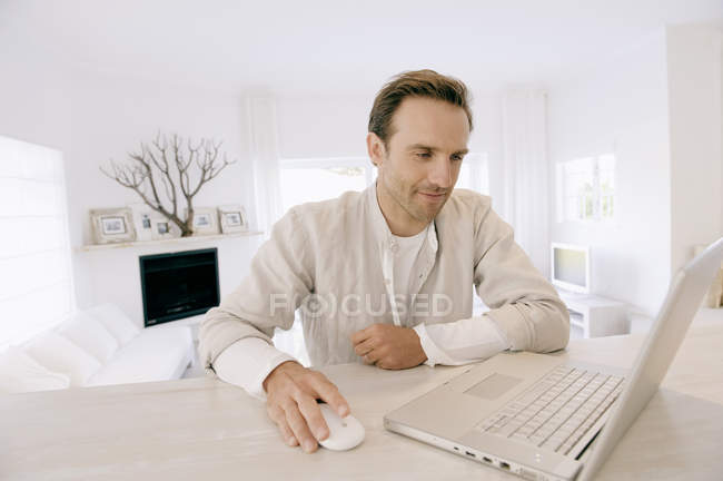 Чоловік працює на ноутбуці і посміхається в сучасній квартирі — стокове фото
