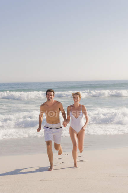 Пара бегущих по песчаному пляжу держащихся за руки — стоковое фото