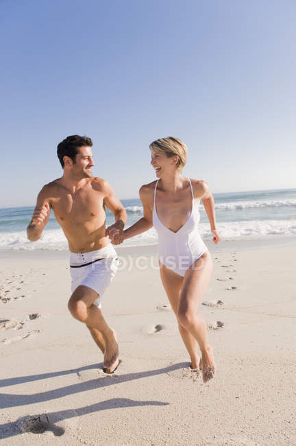 Pareja corriendo en la playa de arena de la mano - foto de stock