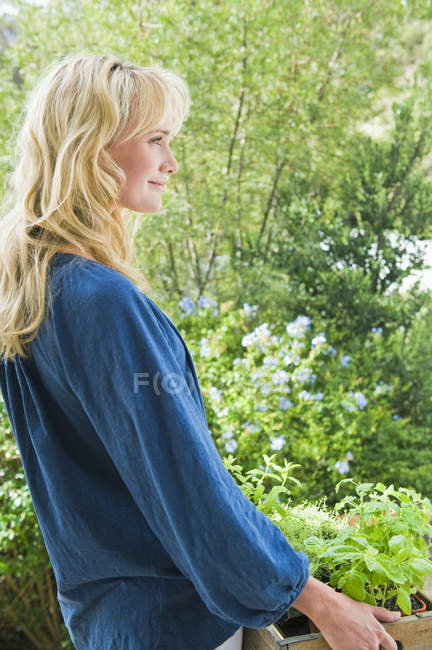 Sonriente mujer llevando cajón de plantas en el jardín - foto de stock