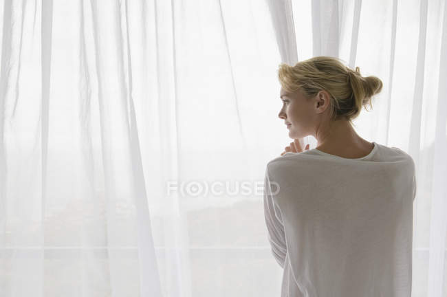 Vista posteriore della donna che apre tenda di balcone a casa — Foto stock