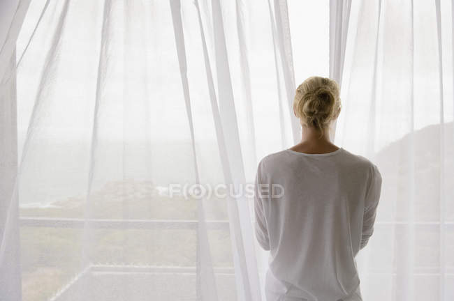 Rear view of woman opening curtain of balcony at home — Stock Photo