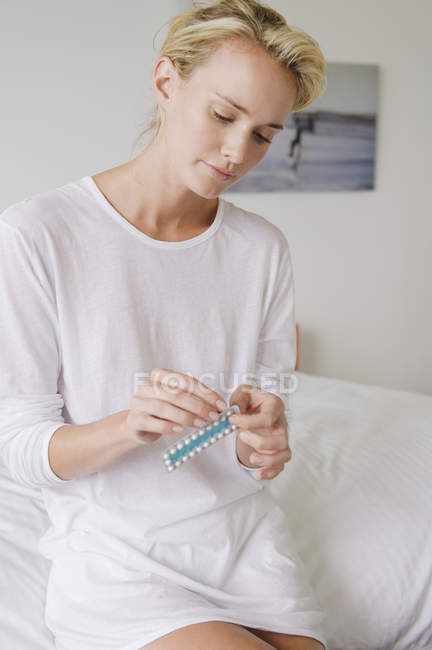 Woman holding blister pack of medicine while sitting on bed — Stock Photo