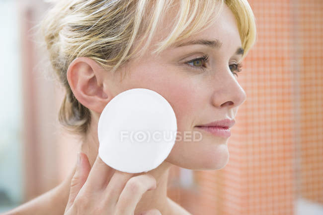 Young woman applying face powder with cotton ball — Stock Photo