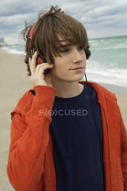 Primer plano del adolescente escuchando música con auriculares en la playa del mar - foto de stock