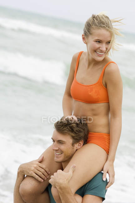 Мужчина несет женщину на плечах на пляже — стоковое фото