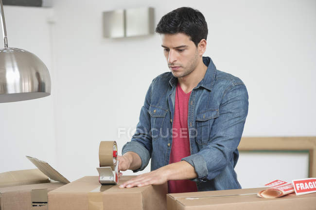 Человек заклеивает картонную коробку в квартире — стоковое фото