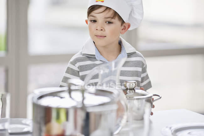 Задумливий маленький хлопчик розміщує сковороди на обідньому столі — стокове фото
