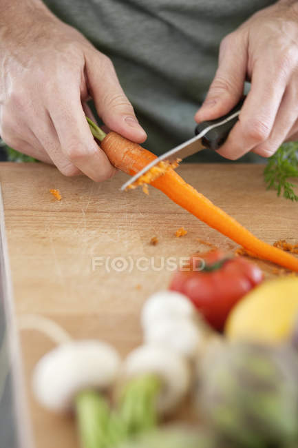 Mãos masculinas cortando cenoura na tábua de corte de madeira — Fotografia de Stock