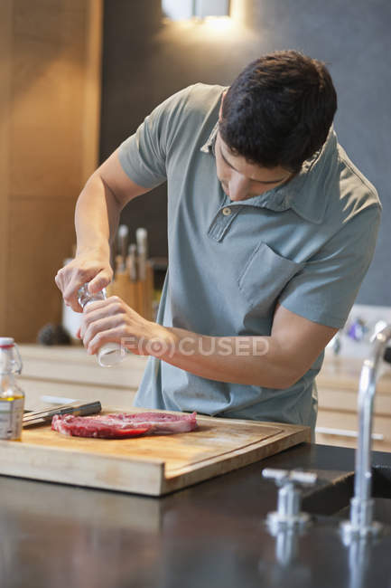 Uomo spruzzando pepe nero sulla carne in cucina moderna — Foto stock