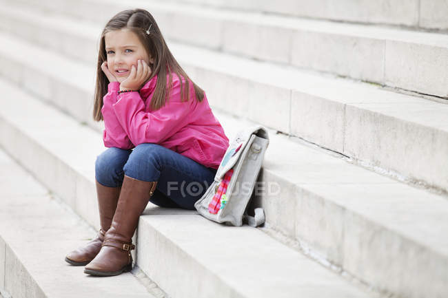 Little dreamy schoolgirl sitting on stairs outdoors — Stock Photo