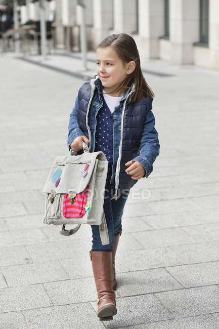 Sorrindo pequena estudante carregando saco escolar enquanto caminhava na rua — Fotografia de Stock