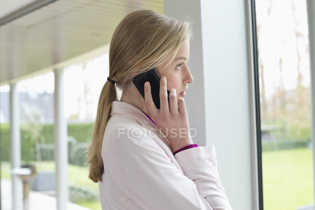 Jovem loira empresária falando no celular ao lado da janela — Fotografia de Stock