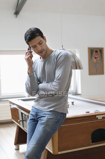 Человек, прислонившийся к бильярдному столу, разговаривая по мобильному телефону — стоковое фото