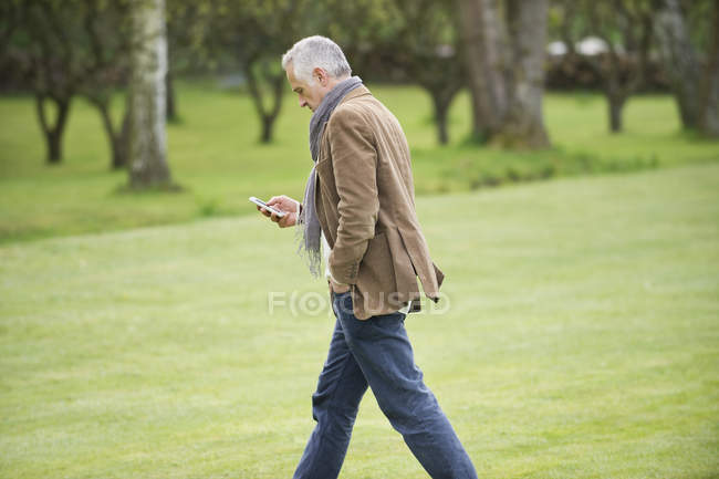 Елегантний чоловік використовує мобільний телефон під час прогулянки в парку — стокове фото