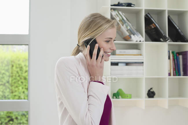 Jeune femme d'affaires blonde souriante parlant sur un téléphone portable au bureau — Photo de stock