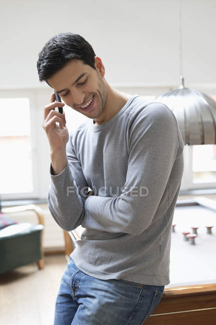 Man leaning on pool table while talking on mobile phone — Stock Photo