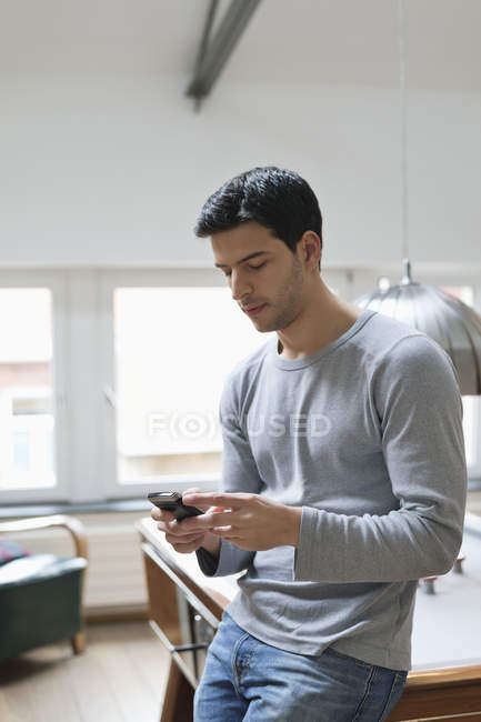 Young man leaning against pool table and using mobile phone — Stock Photo