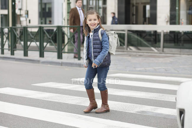 Scolaretta sorridente che attraversa una strada in città — Foto stock