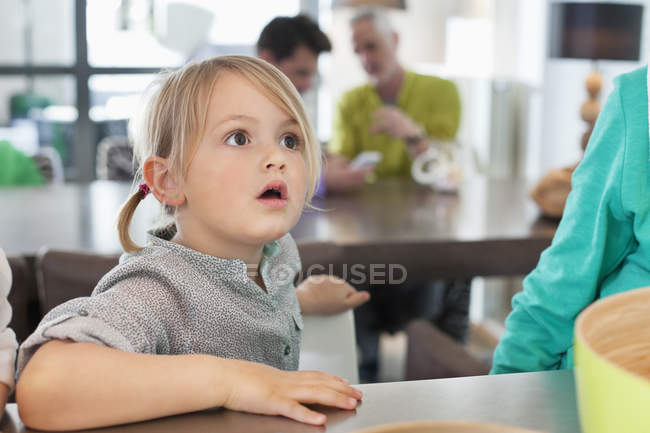 Surprised little girl sitting at table at home — Stock Photo