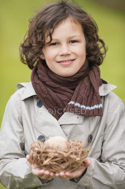 Портрет улыбающегося мальчика, держащего птичье гнездо на улице — стоковое фото
