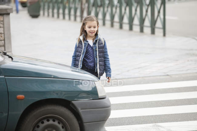 Scolaretta sorridente che attraversa una strada in città — Foto stock